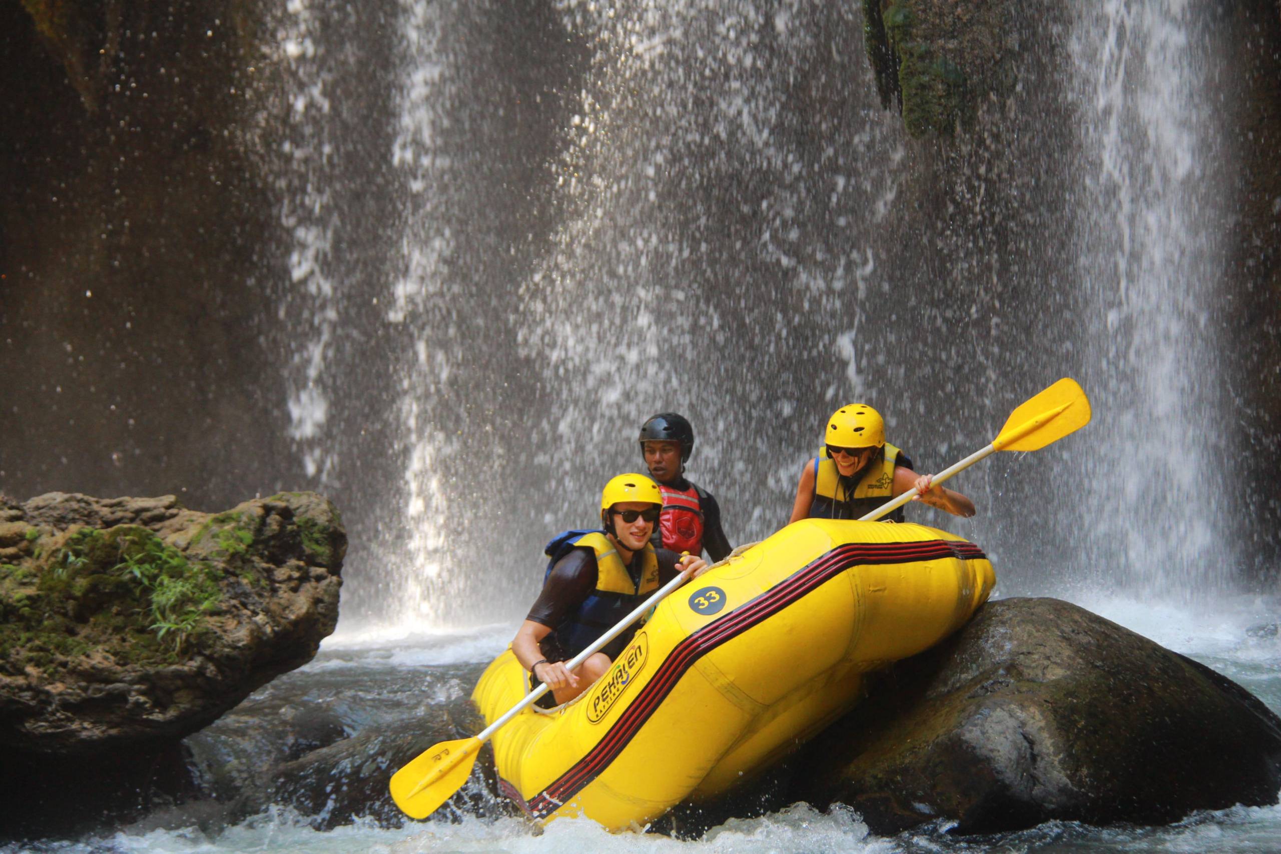 Travellers rafting in a yellow boat beneath a waterfall on the Pekalen River