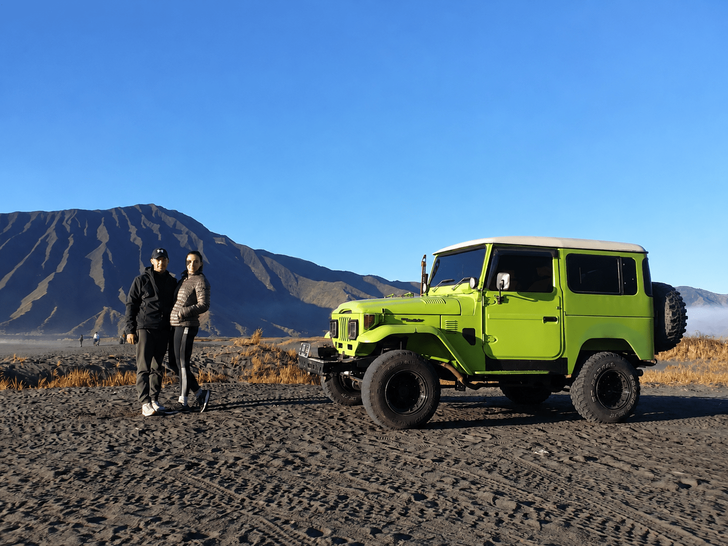 Two travellers beside a green private jeep in the Bromo caldera